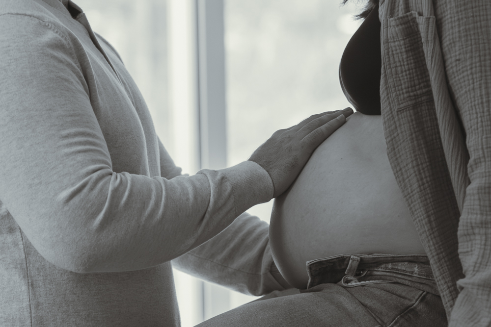 Close-up of a husband's hand gently resting on his wife's pregnant belly during an intimate at-home maternity photoshoot.